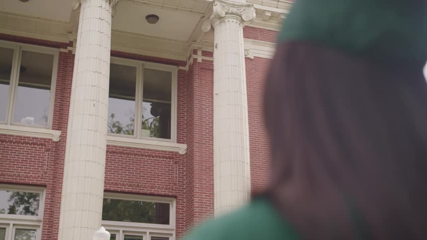 Woman wearing a graduation cap and gown looking at a building