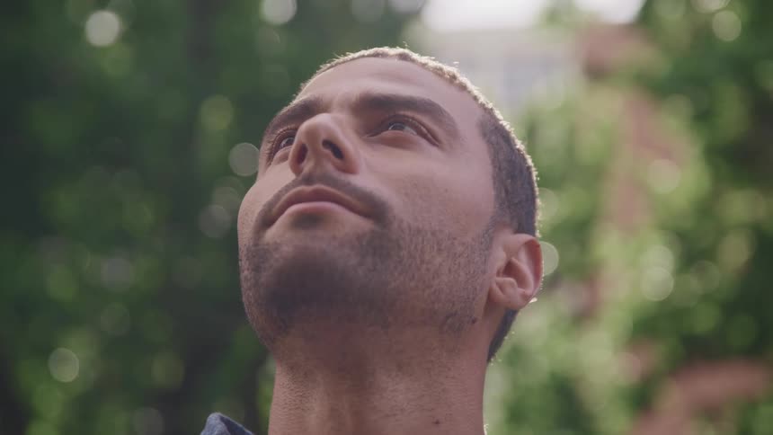 Young man opens his eyes looking up at the sky outdoors