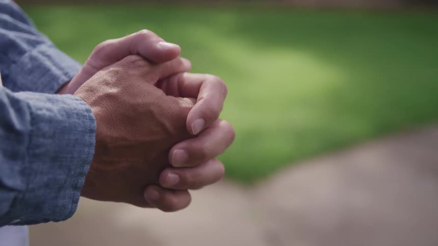 Locked hands of a man resting near the green grass on a park