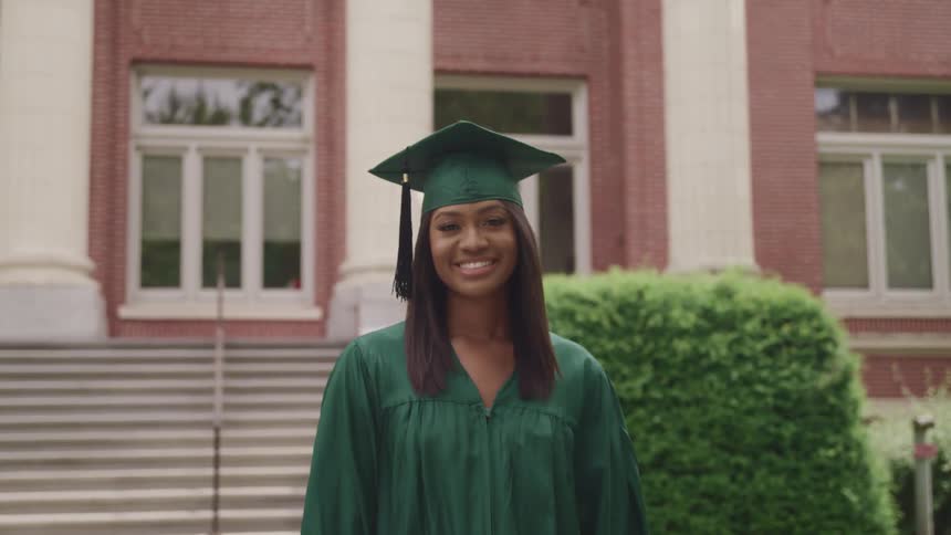 Smiling woman wearing a green graduate dress and hat in front of the university