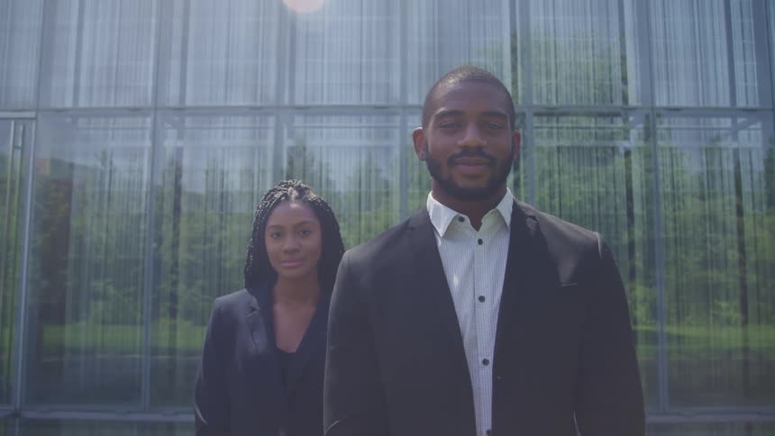 Man and woman in business attire standing outdoors looking at the camera