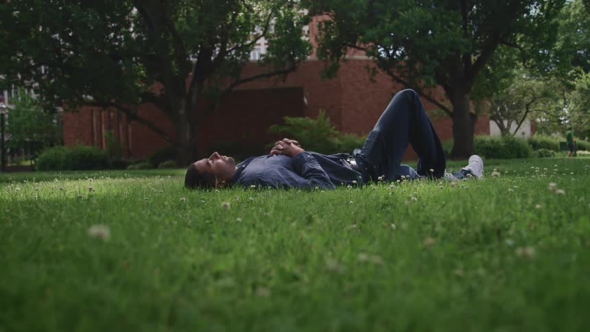 A man lying down and relaxing on a grassy lawn in summer