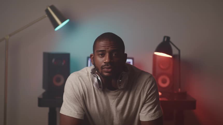 A man with his headphones around his neck looks ahead with speakers behind him
