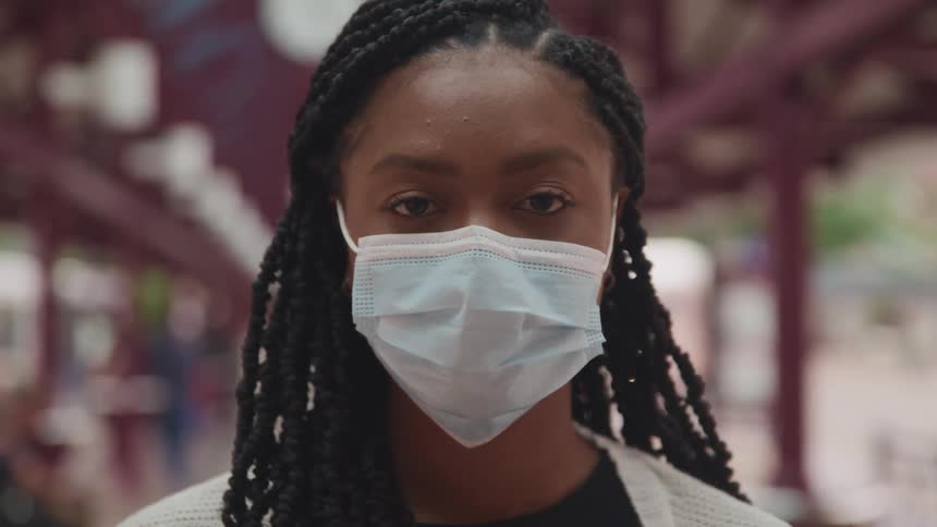 Young woman wearing a blue surgical mask standing outdoors looking at the camera