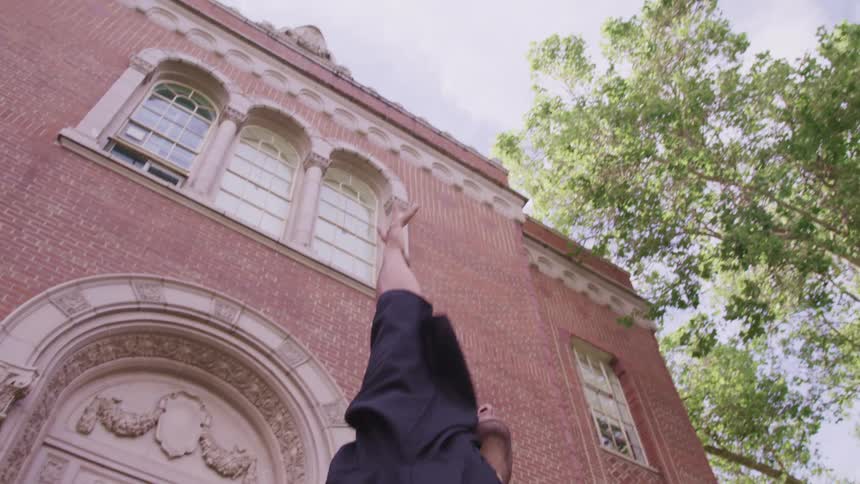 Young man takes off graduation cap and throws it in the air in front of university building