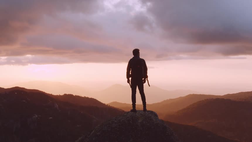 Silhouette of a man standing at the top of a rock outdoors in the mountains