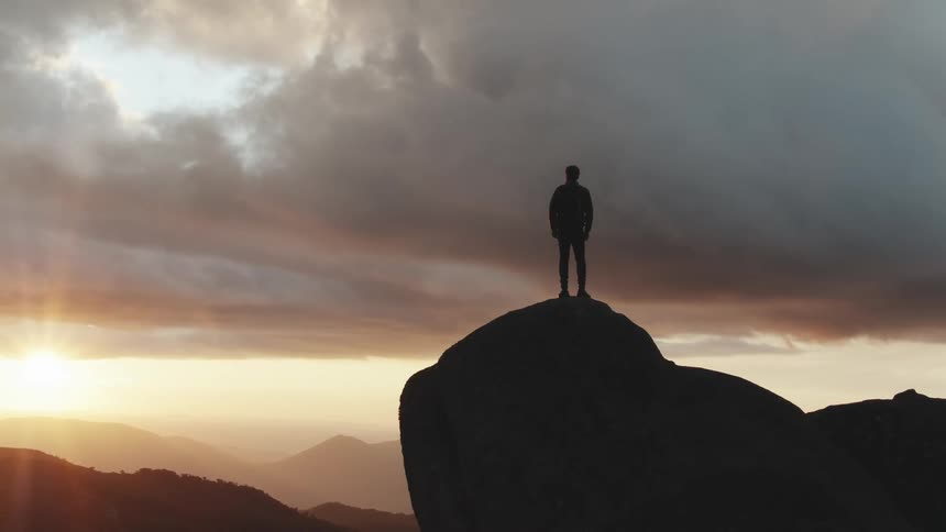 A male standing on a cliff in the mountains