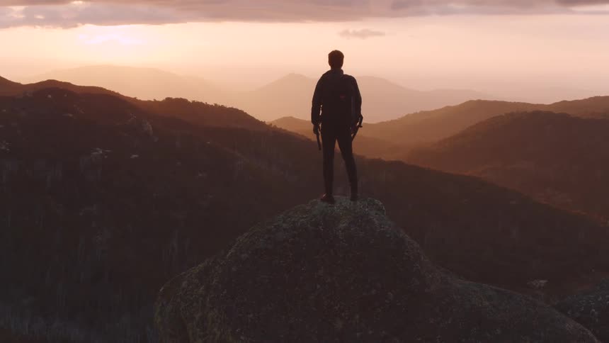A man stands on a mountain summit and look off to the horizon