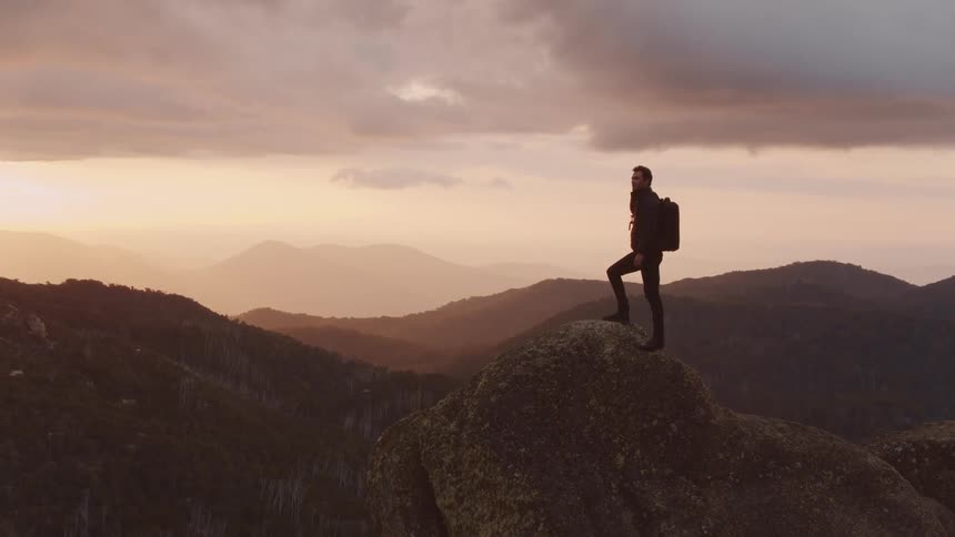 A man stands at the top of a cliff and looks at the landscape