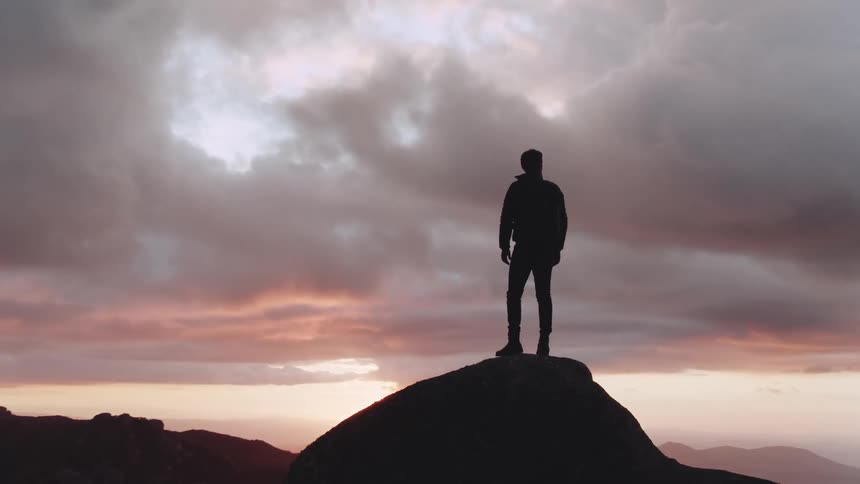 A man standing on a boulder at high altitude and looking at the valley below