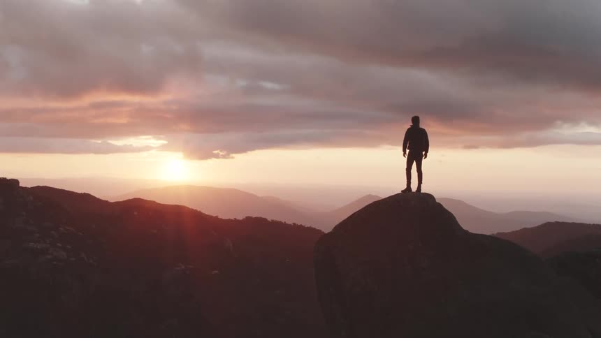 Man climbing top of a mountain at sunset