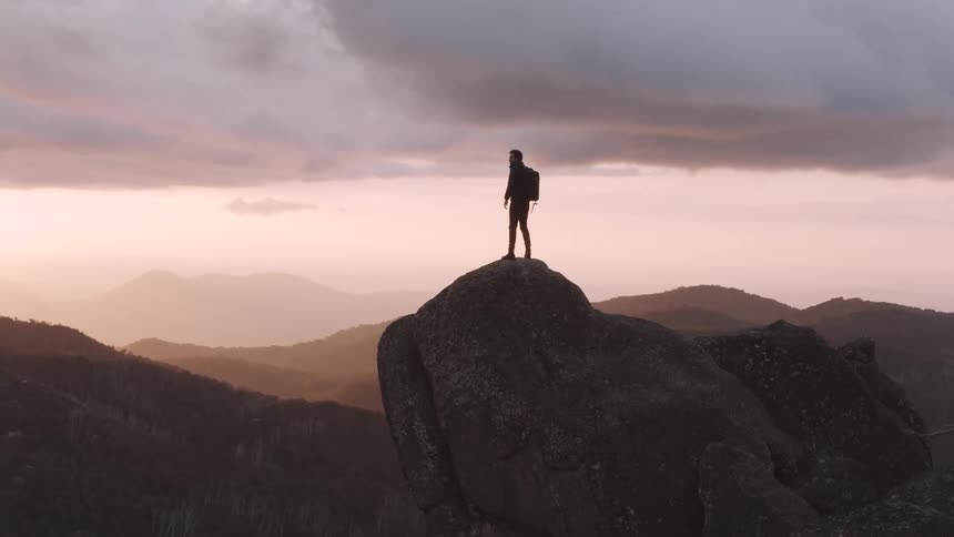 A man standing on a cliff looking at the mountains