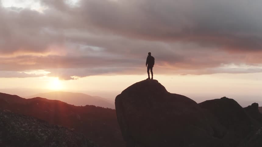 A man with a backpack climbs to the top of a rocky peak