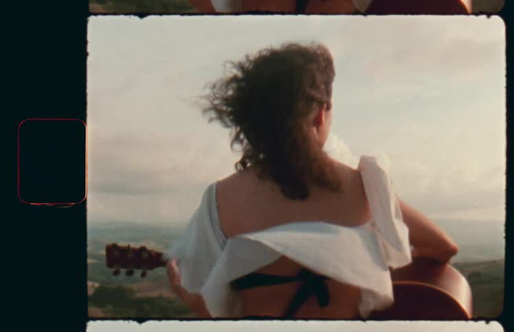 A white woman outdoors holding a guitar in a strong wind