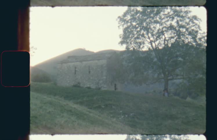 An old stone building sits on a hilltop near a tree