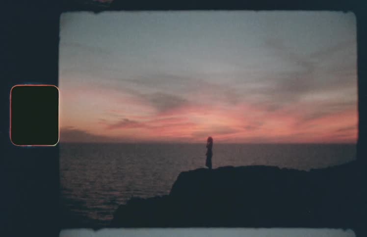 Silhouette of woman in dress standing on rocks near ocean at sunset