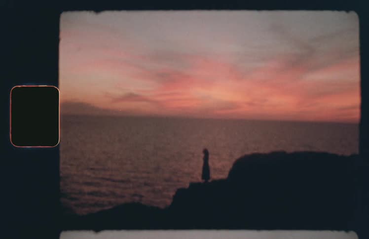 The silhouette of a woman standing on an oceanside cliff at sunset
