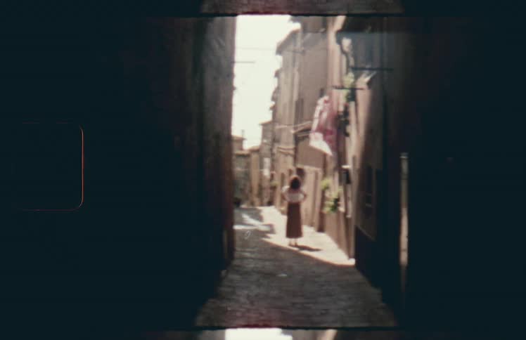 A white woman in a dress stands in a narrow alleyway
