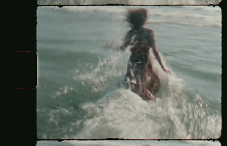 A white woman in a dress runs into the ocean and falls into the water