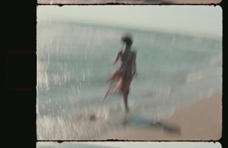 A woman in a dress runs along the beach and into the ocean