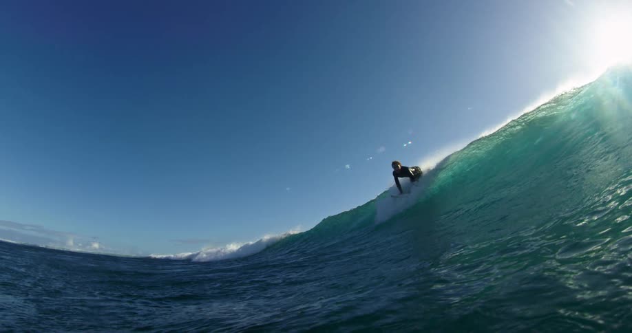 Surfer rides a wave with the sun shining brightly behind him