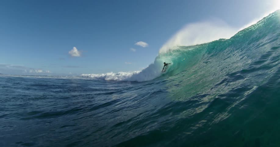 Surfer rides a big splashing wave with the sun shining brightly behind him