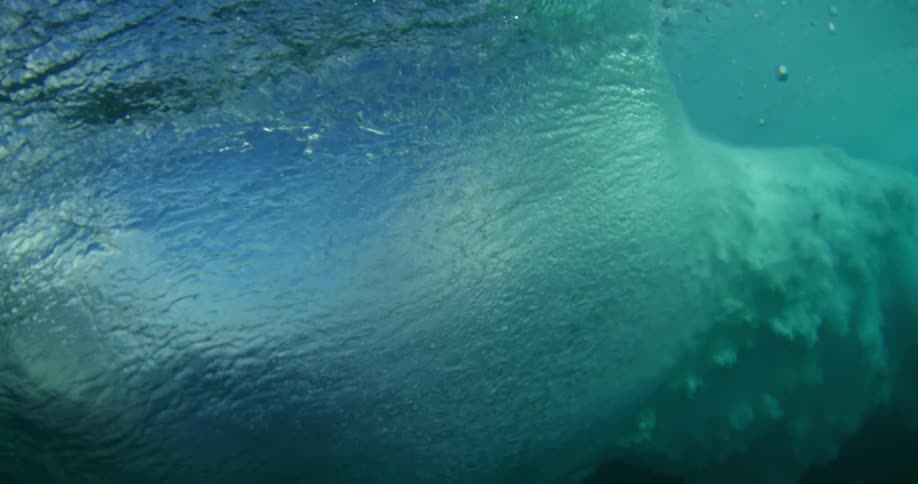 Sun shines on a wave splashing and rolling in overhead and an underwater view