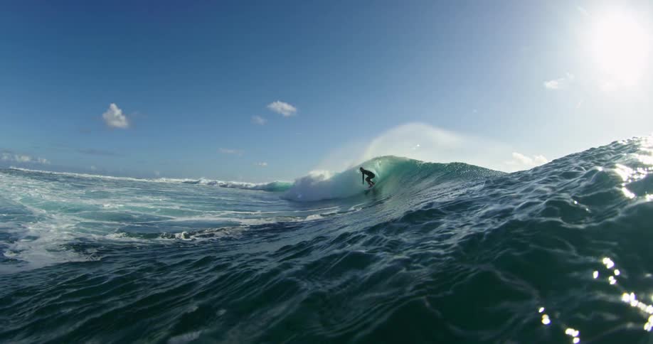 A person surfing on a wave in the ocean with the sky and clouds in the background