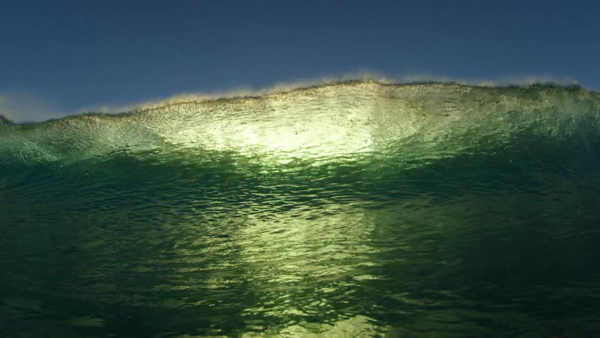 Sun shines on a wave splashing and rolling in overhead and an underwater view