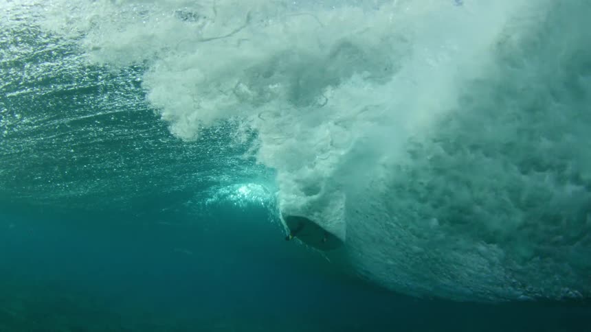 A surfer rides through a tall wave in turquoise ocean water
