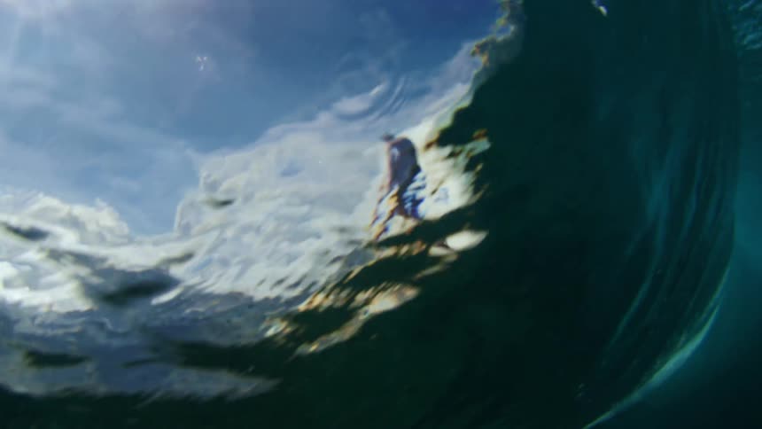Surfer rides a huge wave under a cloudy sky and is seen from underwater
