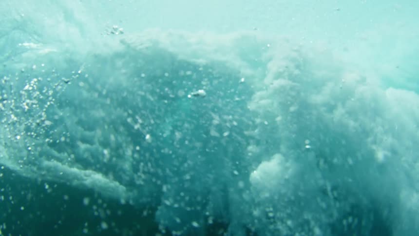 An ocean wave moves across the surface from an underwater view at daytime