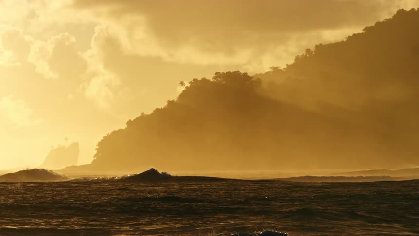 Waves move across the water under and orange sky and land in the distance
