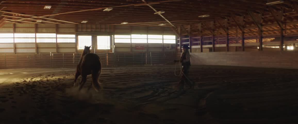 A roped horse bucking and galloping around a cowgirl in a stable