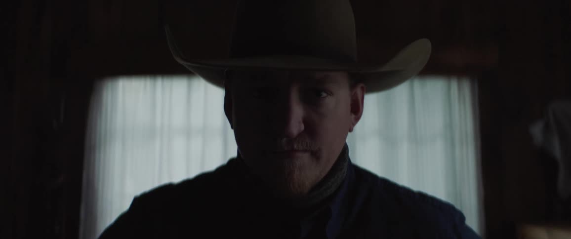 Man with cowboy hat looks at the camera in the dark room