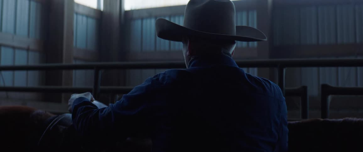 Cowboy saddling a horse inside a dimly lit stable