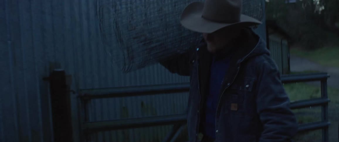 A rancher carries a roll of chicken wire over his shoulder as he walks past a barn