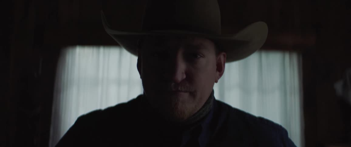 A man in a room with a hat with a wall and window in the background