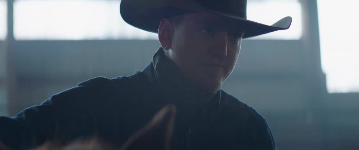 Cowboy standing next to a horse inside a stable