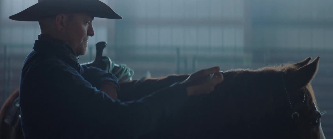 A cowboy saddles his horse in a barn