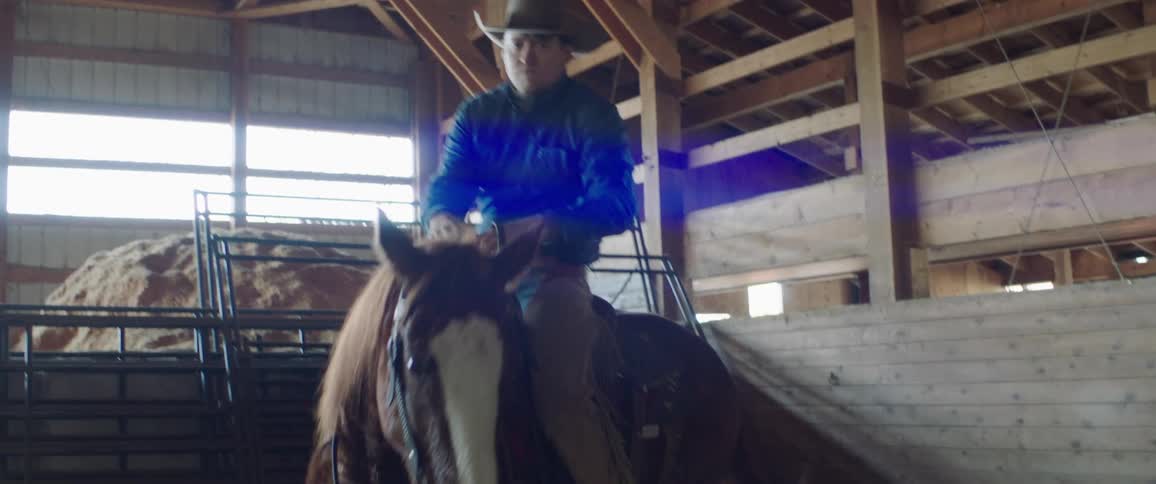 A cowboy mounting a horse inside a stable