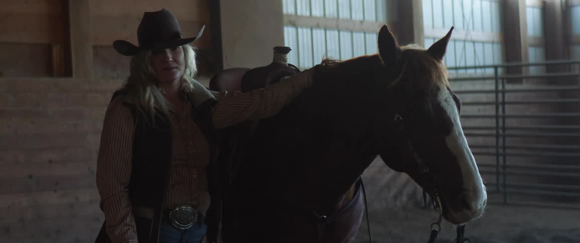 A woman poses for the camera with a horse in a stable during the day