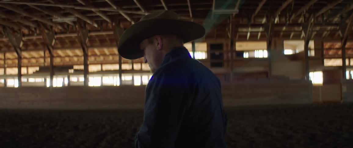 A man with a hat twirling a lasso with walls and windows in the background