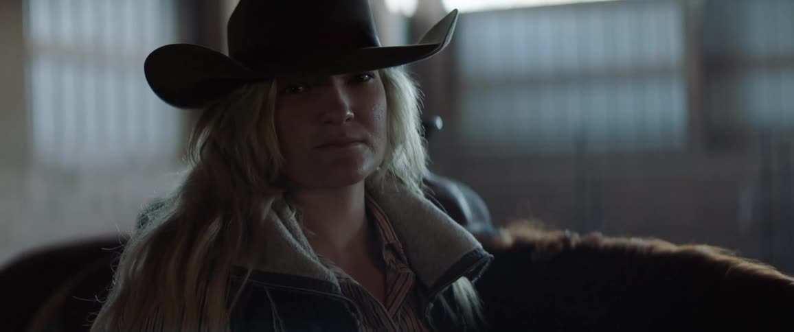 A woman with a jacket and a hat standing next to a horse with walls and windows in the background