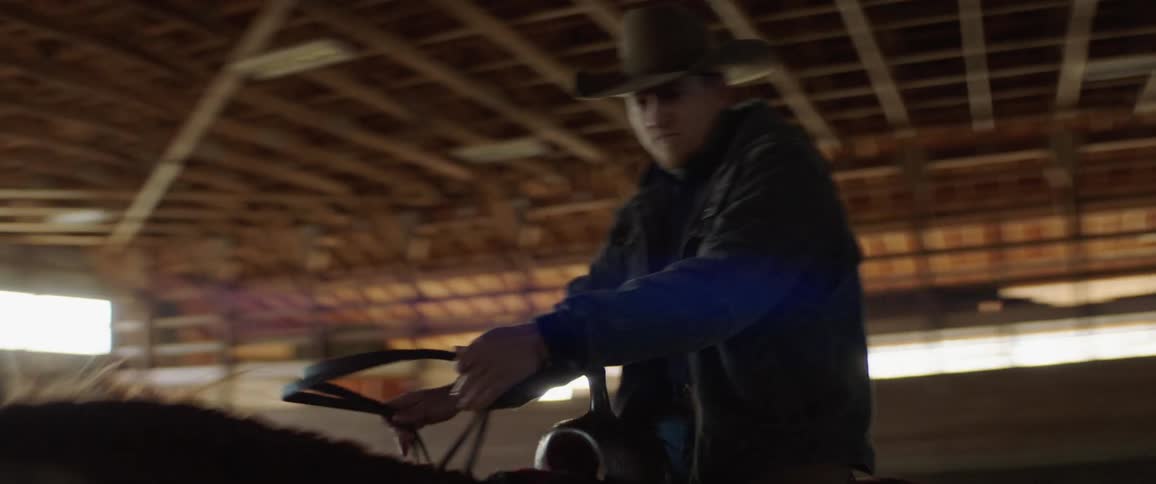 A man rides a horse in a barn while steering it with reins