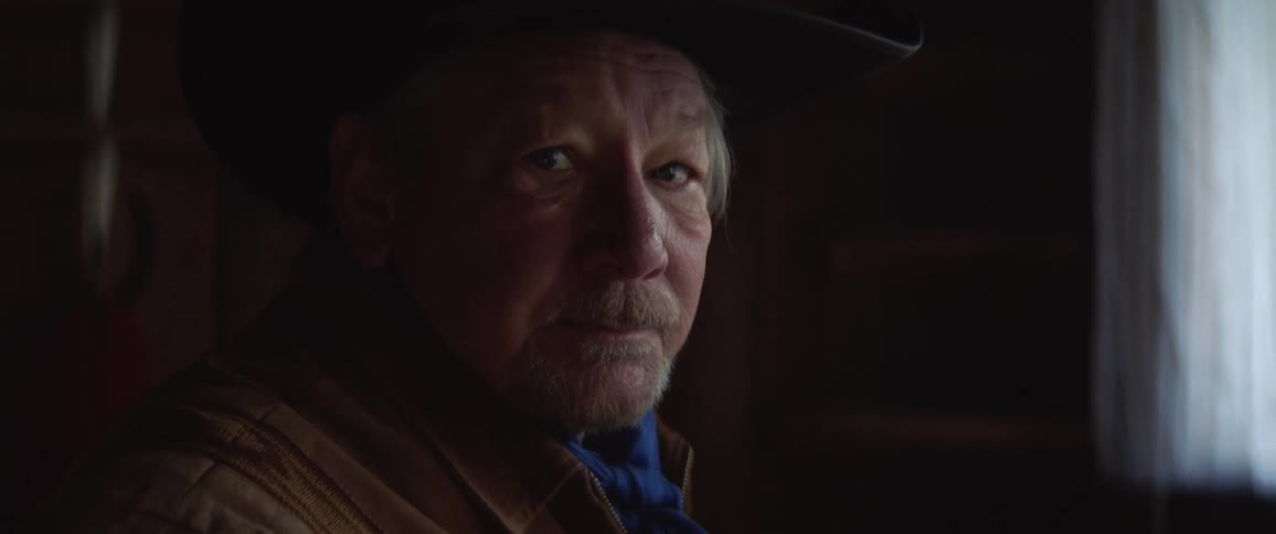 An elderly cowboy in a dark room