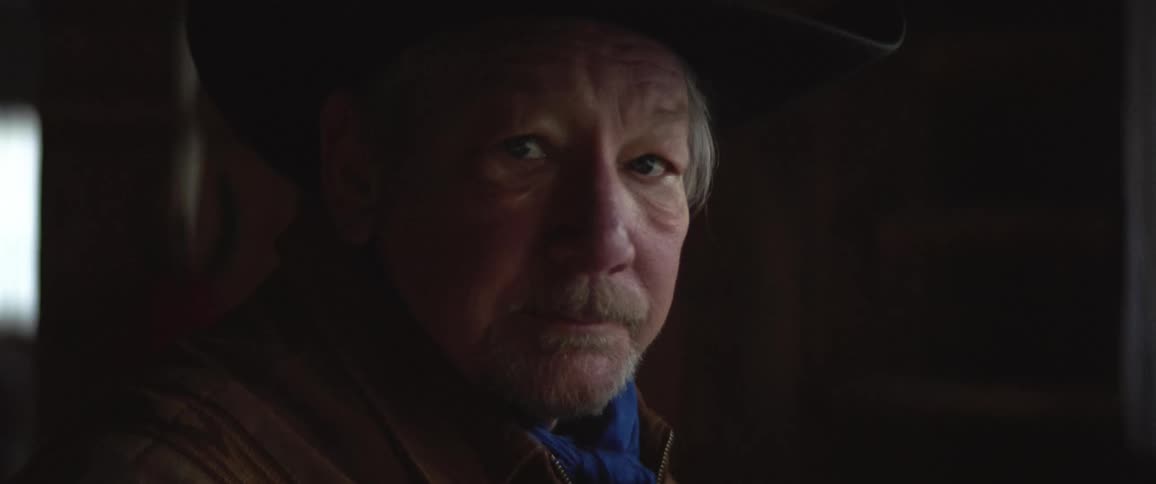 An elderly cowboy wearing a hat looking at the camera