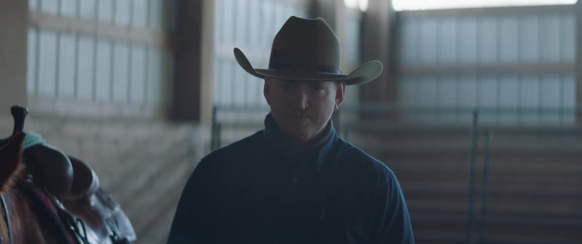 Cowboy standing next to a horse inside a stable