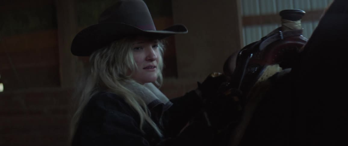 A woman putting a saddle on a horse in a barn