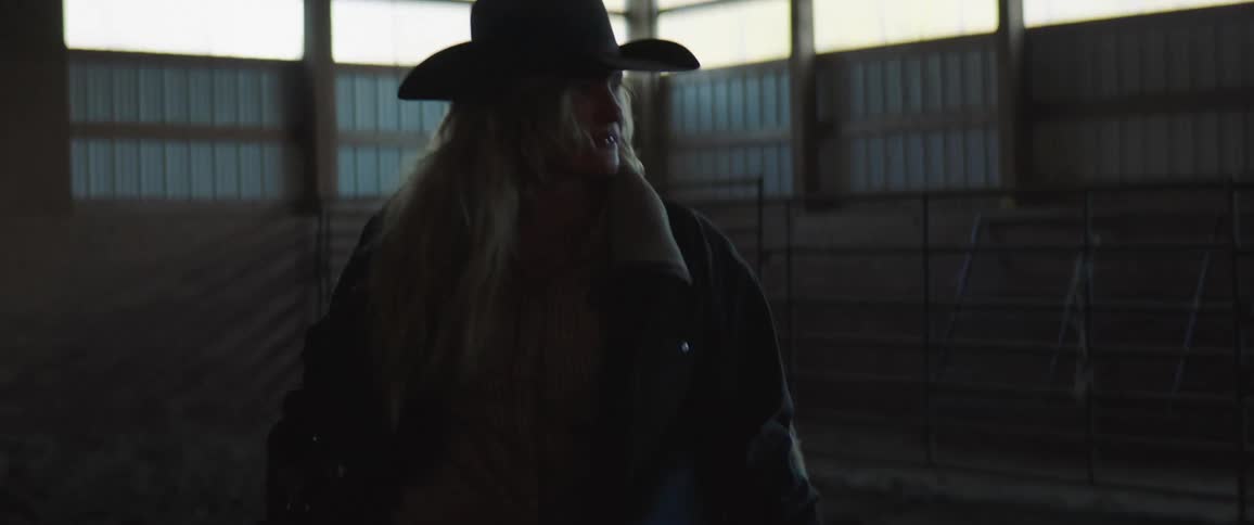 Cowgirl carrying a saddle inside a stable